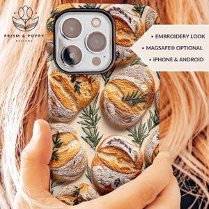 May include: A phone case with an embroidered design of loaves of bread and sprigs of rosemary. The case is available in both iPhone and Android sizes and has an optional MagSafe feature. The text "EMBROIDERY LOOK", "MAGSAFE® OPTIONAL", and "IPHONE & ANDROID" is printed on the case.