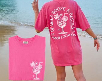 May include: Pink t-shirt with a white graphic of a cocktail with a palm tree and the text "Beagles Booze & Besties 20 Your Location 24" on the back.