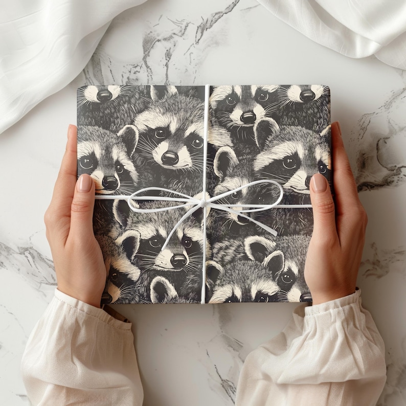 May include: A wrapped gift featuring a repeating pattern of raccoons in black and white. The gift is tied with a white ribbon. The gift is held by a person wearing a white long-sleeved shirt.