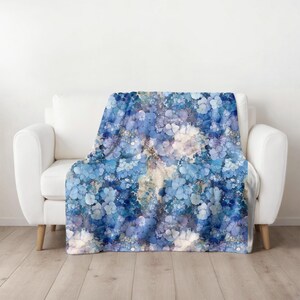 May include: A soft blue and white throw blanket with a floral pattern. The blanket is draped over a white couch.