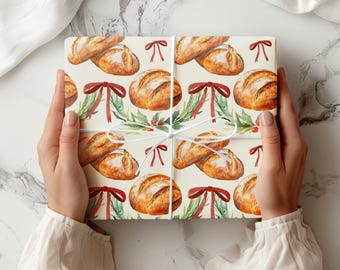 May include: A gift box wrapped in cream-colored paper with a repeating pattern of watercolor bread loaves, baguettes, and red bows. The box is tied with white twine and a sprig of greenery. The overall theme is bakery or holiday.