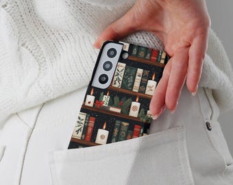 May include: A black smartphone case featuring a bookshelf design with candles, books, and festive greenery. The case has a matte finish and is visible in a white pocket. The design includes red, green, and white elements.