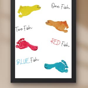 May include: Framed art print featuring colorful footprint fish. The print includes the text "One Fish," "Two Fish," "RED Fish," and "BLUE Fish." Each fish is a different color: yellow, orange, red, and blue. The artwork is in a black frame.
