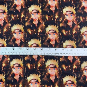 May include: Fabric featuring a repeating pattern of a character with spiky blonde hair, blue eyes, and a black headband. The character is set against a fiery, orange and brown background. The fabric is approximately 12 inches wide.