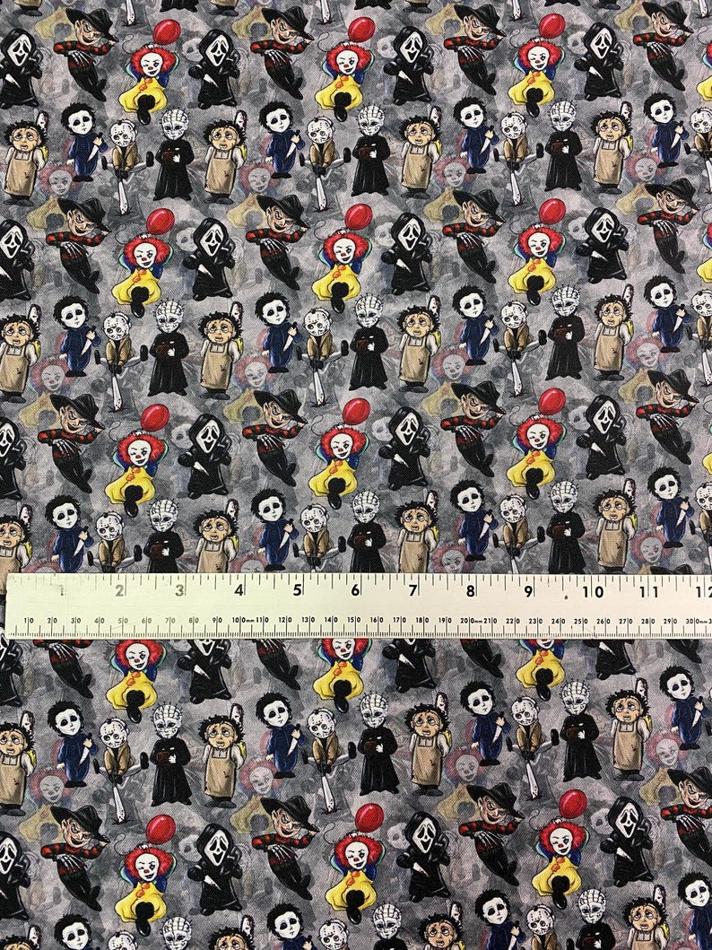 May include: A gray fabric with a repeating pattern of cartoon horror movie characters, including Pennywise, Ghostface, and Freddy Krueger. The design features a ruler with inch measurements.