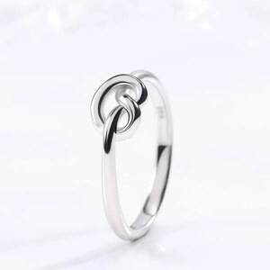 May include: A silver ring featuring a knot design. The knot is a simple, elegant design that is perfect for everyday wear.