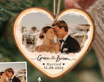 May include: Heart-shaped wooden ornament featuring a wedding photo of a couple. The ornament has a light-colored wood grain border and a photo of a bride and groom. The text "Grace & Brian" and "Married 12.06.2025" are also visible.