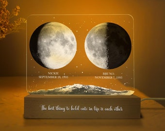 May include: A wooden base with a clear acrylic panel featuring two crescent moons with the names "Nickie" and "Bruno" and their birthdates "September 28, 1993" and "November 7, 1993". The text "The best thing to hold onto in life is each other" is printed on the wooden base.