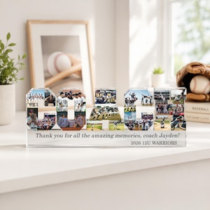 May include: A clear acrylic baseball-themed COACH sign filled with team photos. The sign includes the text "Thank you for all the amazing memories, coach Jayden! 2026 12U WARRIORS". A baseball glove and ball are visible in the background.