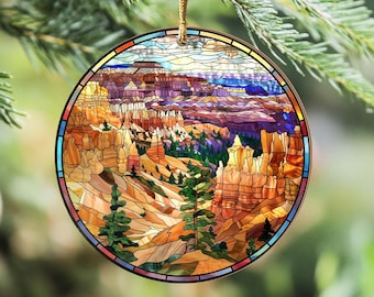Puede incluir: Un adorno redondo de vidrio tintado que representa una escena colorida del Parque Nacional Bryce Canyon en Utah. El adorno muestra un paisaje de formaciones rocosas rojas, árboles y un cielo azul.