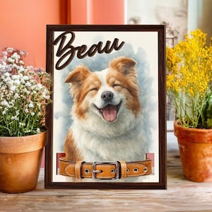 May include: A framed watercolor print featuring a smiling dog with brown and white fur, named "Beau" in script. The print includes a brown leather dog collar with a silver buckle. The artwork is displayed with potted plants.