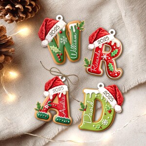 Pu&ograve; includere: Quattro decorazioni natalizie a forma di lettere, ognuna con un cappello da Babbo Natale e l'anno 2025. Le lettere sono decorate con glassa rossa e verde, agrifoglio e fiocchi di neve. I nomi sono scritti su ogni lettera.