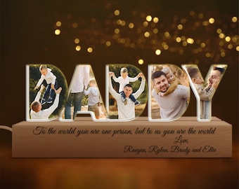 Puede incluir: Un letrero luminoso de madera que deletrea "DADDY" con fotos de un padre y sus hijos en cada letra. El letrero tiene el texto "To the world you are one person, but to us you are the world Love, Raegan, Rylan, Brody and Ellie" en la base.