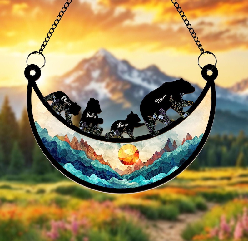 May include: A crescent moon-shaped metal wind chime with a mountain and sunset scene.  Silhouettes of bears with the names "Mom", "Olivia", "Jake", and "Liam" are walking across the moon.
