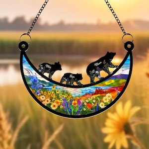 May include: A stained glass crescent moon suncatcher with a colorful floral design and three black bear silhouettes. The bears are walking across the moon and each has a name written on it: Mia, Ben, and Mom.