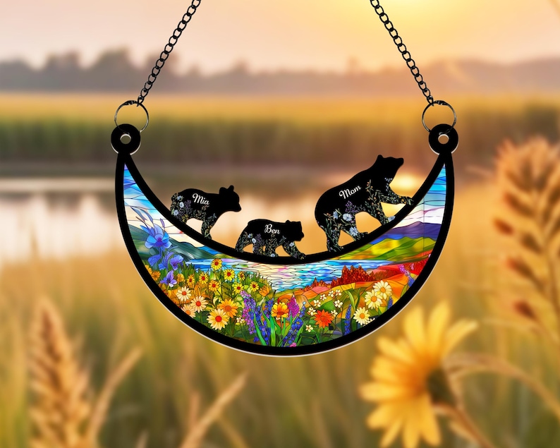 May include: A stained glass crescent moon suncatcher with a colorful floral design and three black bear silhouettes. The bears are walking across the moon and each has a name written on it: Mia, Ben, and Mom.