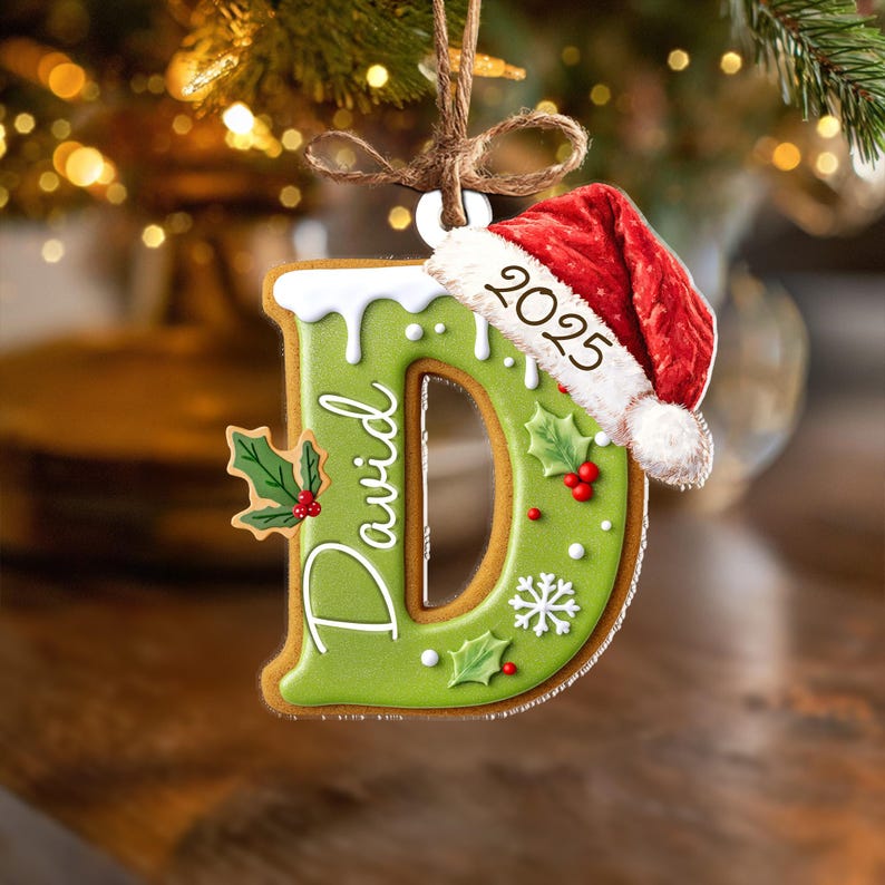 Pu&ograve; includere: Un ornamento natalizio a forma di lettera "D" con il nome "David" scritto sopra. L'ornamento &egrave; verde con glassa bianca, decorazioni di agrifoglio e un cappello da Babbo Natale con "2025". Appeso a un filo marrone.