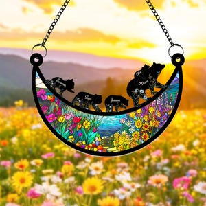 May include: A crescent moon-shaped stained glass suncatcher with a floral design and five black bear silhouettes. The bears are walking in a line and each has a name written on it: Emma, Leo, Jason, Mom, and Alex.