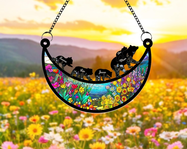 May include: A crescent moon-shaped stained glass suncatcher with a floral design and five black bear silhouettes. The bears are walking in a line and each has a name written on it: Emma, Leo, Jason, Mom, and Alex.
