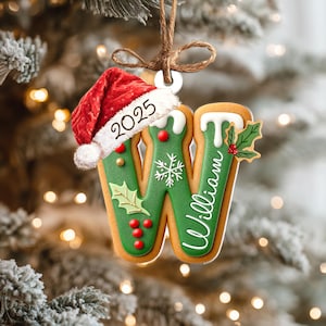 Pu&ograve; includere: Un ornamento natalizio a forma di lettera &laquo;W&raquo; con il nome &laquo;William&raquo; scritto sopra. L'ornamento verde presenta dettagli in glassa bianca, agrifoglio e bacche rosse. Un piccolo cappello di Babbo Natale con &laquo;2025&raquo; &egrave; attaccato. &Egrave; appeso a una corda marrone.