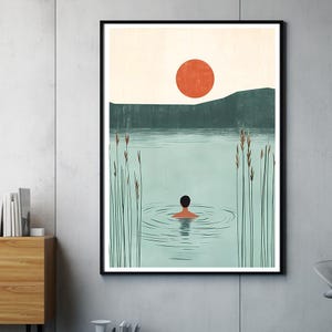 Könnte beinhalten: Gerahmter Kunstdruck, der eine ruhige Seeszene darstellt. Eine Person schwimmt im Wasser, mit einer großen orangefarbenen Sonne am Himmel. Hohe Schilfgräser säumen das Ufer. Das Kunstwerk ist in einem schwarzen Rahmen gerahmt.