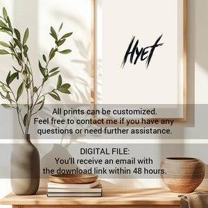 Puede incluir: Una impresi&oacute;n enmarcada con la palabra "HYET" escrita en tinta negra sobre un fondo blanco. La impresi&oacute;n se muestra en una mesa de madera con un jarr&oacute;n de vegetaci&oacute;n y un cuenco decorativo.