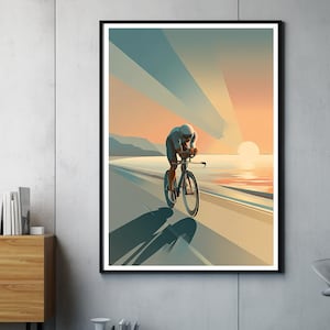 Könnte beinhalten: Ein gerahmter Kunstdruck zeigt einen Radfahrer in aerodynamischer Position auf einer Straße neben dem Meer. Das Kunstwerk verwendet Blau-, Orange- und Gelbtöne, um eine Sonnenuntergangsszene zu schaffen. Der Schatten des Radfahrers erstreckt sich über die Straße.