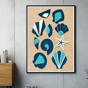 Könnte beinhalten: Ein gerahmter Wandkunstdruck mit einer Sammlung stilisierter Muscheln und einem Seestern auf einem strukturierten beigen Hintergrund. Die Formen bestehen aus geschichteten Papierausschnitten in Dunkelblau, Hellblau und Weiß.