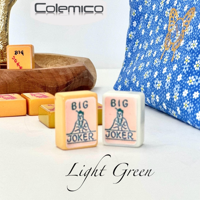 May include: Mahjong tiles with "BIG JOKER" text and a graphic of a figure. The tiles are light orange and white. A blue floral patterned bag is in the background. The word "Colemico" is at the top. The words "Light Green" are at the bottom.
