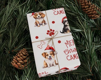 May include: Wrapped gift with a festive dog-themed Christmas design. The white wrapping paper features illustrations of puppies wearing Santa hats, paw prints, and the words "Merry Christmas Came". The gift is tied with twine and set on a bed of pine needles.