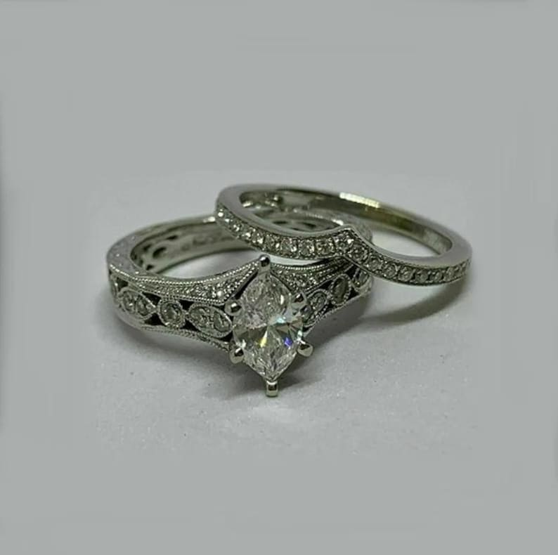 May include: A silver engagement ring set with a large marquise-shaped diamond and smaller diamonds set in a delicate filigree design.