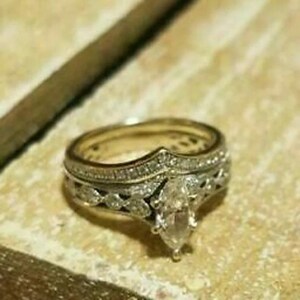 May include: A gold engagement ring set with a marquise-shaped diamond center stone and smaller diamonds on the band. The ring is set on a brown surface.