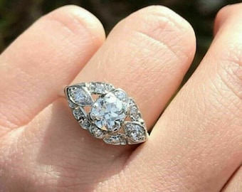 May include: A silver ring with a large, round, clear diamond surrounded by smaller diamonds in a leaf-like design.