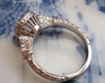 Peut inclure: Une bague de fiançailles en argent avec des détails gravés complexes sur la bande et une grande pierre précieuse ronde sertie à griffes.