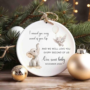 May include: White ceramic Christmas ornament with a gray elephant illustration and the text "I carried you every second of your life and we will love you every second of us Our sweet baby November 2024".