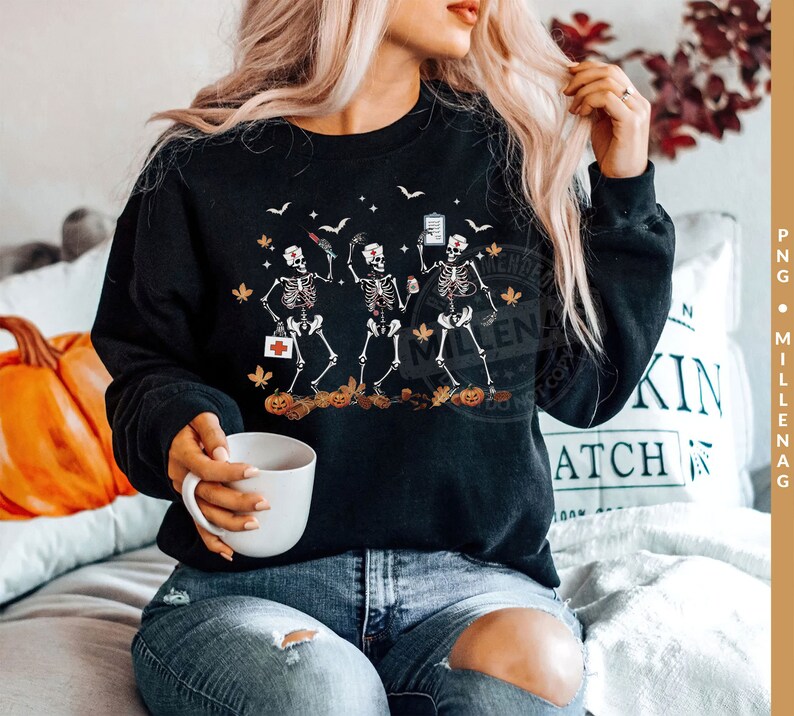 May include: A black sweatshirt with a graphic of three skeletons dressed as nurses holding medical supplies and pumpkins. The skeletons are wearing nurse hats and holding a clipboard, a syringe, and a bottle of pills. The text "Boo Crew" is printed on the sweatshirt.
