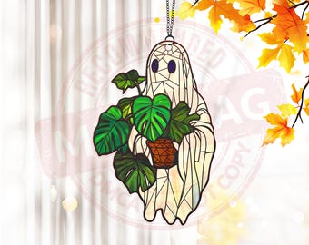May include: A stained glass ornament featuring a white ghost holding a potted plant with green leaves. The ghost has a geometric pattern and black eyes.