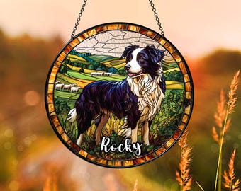 May include: A stained glass window hanging with a black and white border collie dog standing in a green field with sheep. The dog is looking to the left and the text "Rocky" is written below the dog.