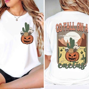 May include: White t-shirt with a graphic of a jack-o-lantern in a cactus pot on the front and the text "Go Fall On A Cactus" on the back.
