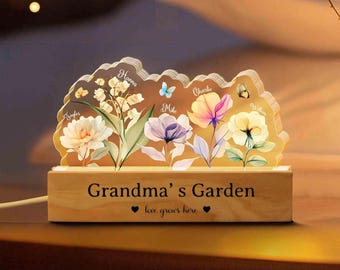 May include: A decorative wooden night light with a floral design. The light features a wooden base with the text "Grandma's Garden" and a floral arrangement with names. The flowers are in shades of white, pink, purple, and yellow.