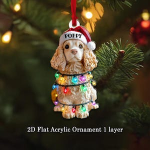 May include: A Christmas tree ornament shaped like a dog wearing a Santa hat with the name "POPPY". The dog is wrapped in colorful Christmas lights. The ornament is made of acrylic and has the text "2D Flat Acrylic Ornament 1 layer".