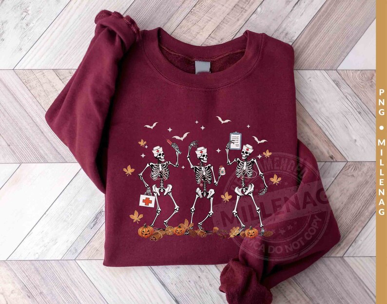 May include: A maroon sweatshirt with a graphic of three skeletons dressed as nurses. The skeletons are holding medical supplies and a cup of coffee. The graphic is surrounded by fall leaves and pumpkins.