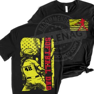 May include: Black t-shirt with a yellow and red graphic of a softball player with the text "Softball Dad" and the number "42" on the player's jersey. The player is standing in front of an American flag.