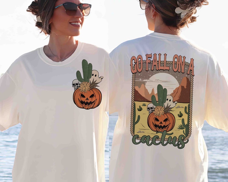 May include: White t-shirt with a graphic of a jack-o'-lantern in a cactus pot with a ghost and skulls. The back of the shirt has the text "Go Fall On A Cactus" with a graphic of a jack-o'-lantern in a cactus pot with a ghost and skulls.