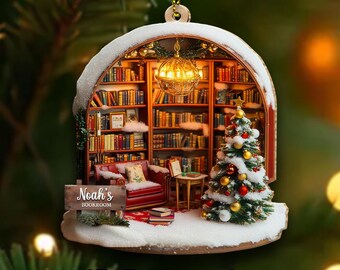 May include: A 2D flat wood Christmas ornament featuring a miniature library scene. The ornament includes a Christmas tree, a red armchair, bookshelves, and a sign that reads "Noah's Bookroom". The ornament is decorated with snow and a hanging gold-colored light.