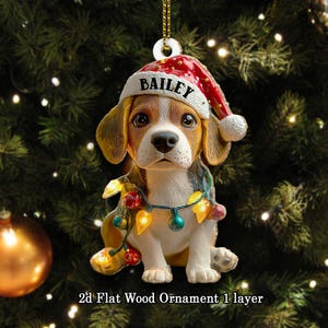 May include: A 2D flat wood Christmas ornament featuring a beagle wearing a Santa hat with the name "Bailey" and a string of colorful lights. The ornament is hanging in front of a Christmas tree.