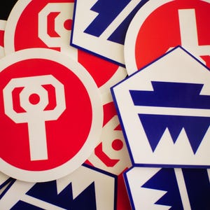 May include: A collection of red and white circular stickers and white and blue pentagonal stickers. The circular stickers feature a white key-like design on a red background. The pentagonal stickers have a blue geometric design on a white background.