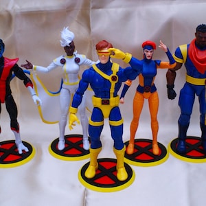 Pode incluir: Um conjunto de seis figuras de ação de personagens dos X-Men. Cada figura está em uma base redonda com um design vermelho e amarelo. As figuras usam trajes azuis, amarelos, brancos e vermelhos.