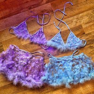 May include: Two sets of lingerie with butterfly designs. One set is light blue and the other is purple. Both sets have a matching bra and skirt with a fluffy trim.