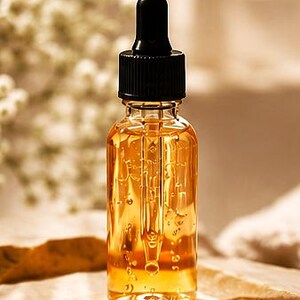 K&ouml;nnte beinhalten: Eine klare Glastropfflasche gef&uuml;llt mit einer gold-bernsteinfarbenen Fl&uuml;ssigkeit. Die Flasche verf&uuml;gt &uuml;ber einen schwarzen Schraubverschluss mit einer integrierten Glastropfpipette, die bis in die Mitte des Beh&auml;lters reicht. Die Fl&uuml;ssigkeit ist viskos.